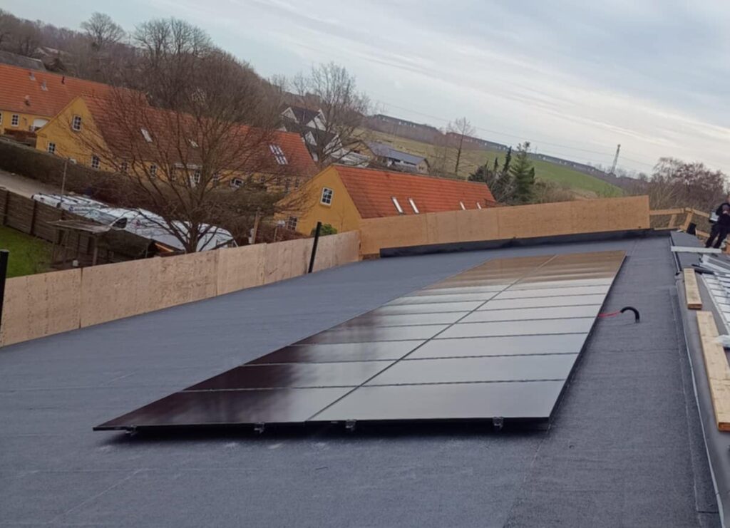 Solpaneler installeret på fladt tag overfor gul bygning