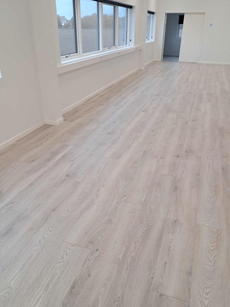 Lyst trægulv i tomt rum med store vinduer.