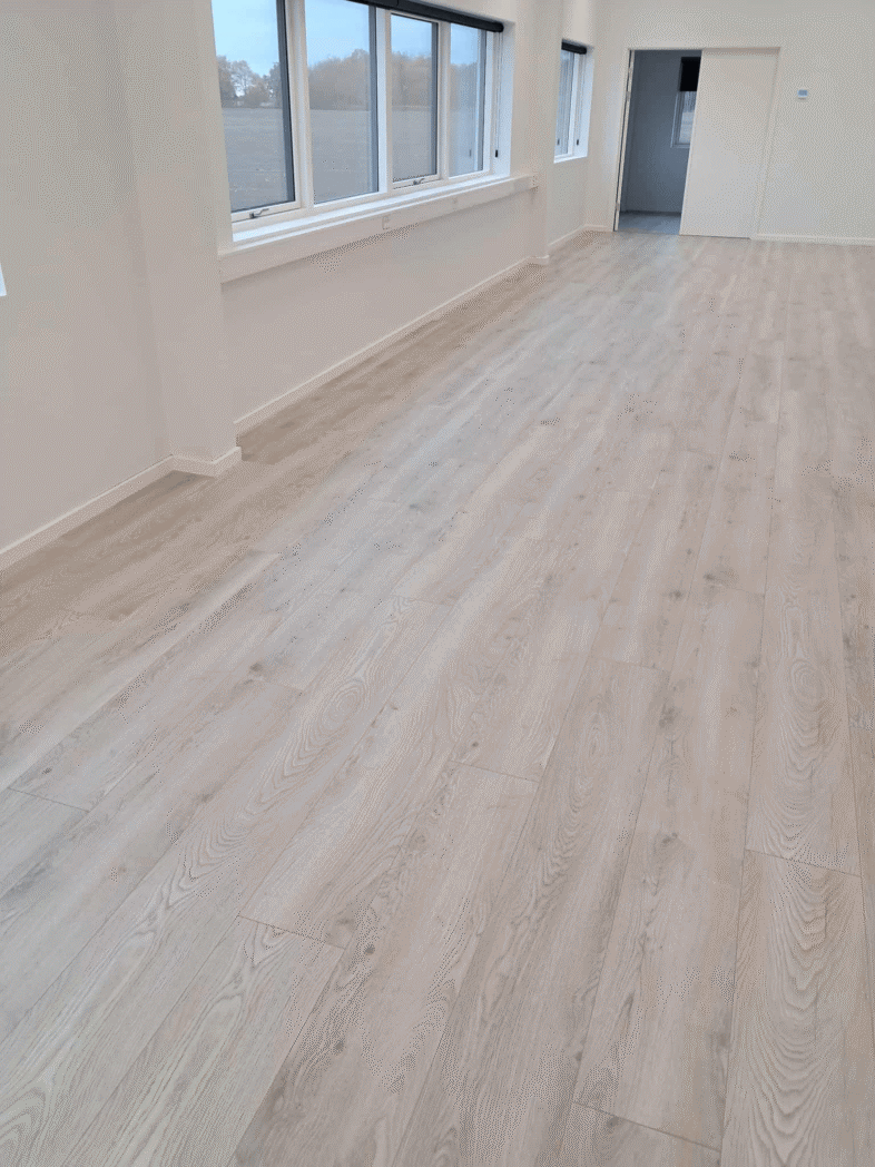 Lyst trægulv i tomt rum med store vinduer.